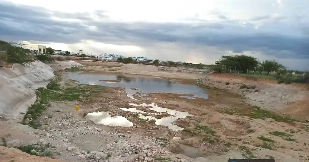 The same kind of earth catchment reduced to shallow pools and cracked pale mud across its floor.